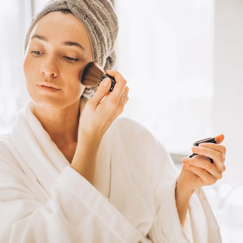 Young woman applying blush and looking into the mirror Young woman applying blush and looking into the mirror
